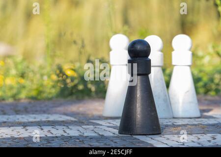 Vier lebensgroße Schachfiguren auf einem Schachbrett, drei weiße und eine schwarze auf der Vorderseite, konzentrieren sich auf die schwarze Spielfigur Stockfoto