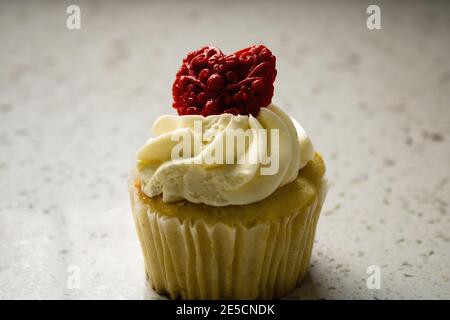 Nahaufnahme von Vanille Cupcake mit weißer Buttercreme-Vereisung mit Gemustertes rotes Fondant Herz für valentinstag Stockfoto