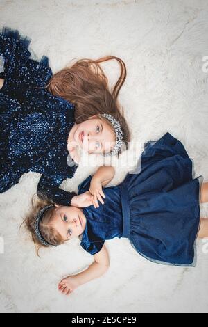 Zwei niedliche Mädchen Schwestern mit blauen Augen liegen auf Ihre Rücken in blauen Kleidern auf Kunstfell Stockfoto