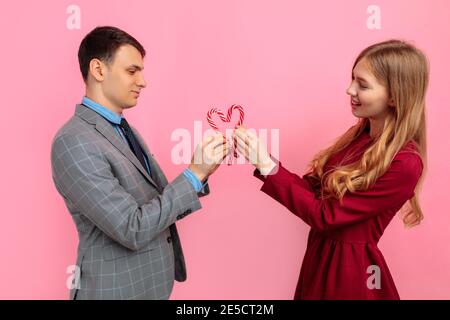 Verliebte Paare, Mann und Frau, machen Sie ein Herz aus Weihnachten gestreiften Süßigkeiten auf einem rosa Hintergrund, feiern Valentinstag Stockfoto
