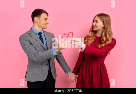 Verliebte Paare, Mann und Frau, machen Sie ein Herz aus Weihnachten gestreiften Süßigkeiten auf einem rosa Hintergrund, feiern Valentinstag Stockfoto