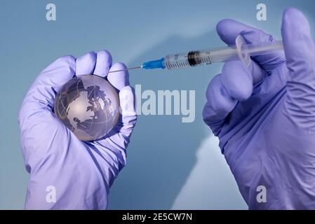 Die Hände der Frau in medizinischen Handschuhen halten einen Planeten Erde Globus und eine Spritze, das Konzept der Impfung. Stockfoto