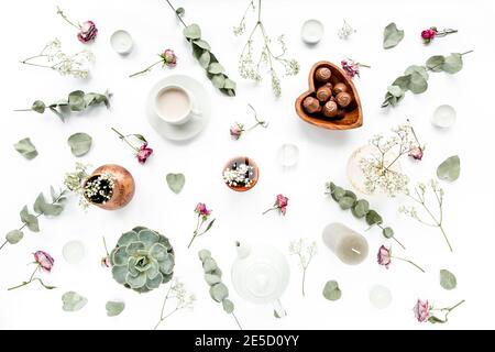 Arbeitsbereich mit Rosenknospen, Eukalyptus-Blätter, saftig, Tee, Tasse Kakao, Süßigkeiten auf weißem Hintergrund. Flach liegend, Ansicht von oben, Arbeitsplatz im Home Office Stockfoto