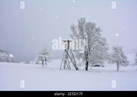 Ein Hunters hoher Sitz aus Holz in einer Landschaft im Winter, mit Bäumen und viel Schnee und Schneefall Stockfoto