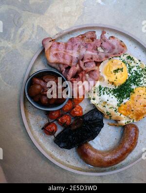 Englisches Frühstück mit Spiegeleiern, Speck, gebratenen Tomaten, gebratenen Pilzen, gebackenen Bohnen, Petersilie und Schweinewurst Stockfoto