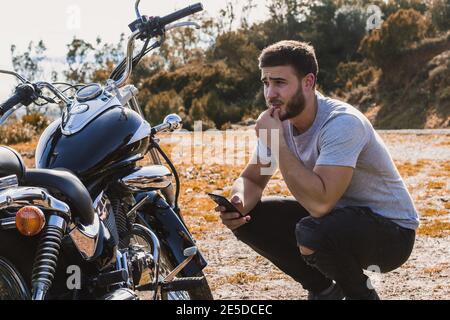 Crouching Biker besorgt über eine Motorrad-Panne Stockfoto