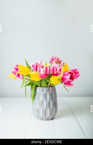 Frisches Frühlingsgelb und rosa Tulpenstrauß in blauer Vase auf weißem Holztisch mit weißem Hintergrund. Festliche Blumen für Mutter, Frauentag Stockfoto