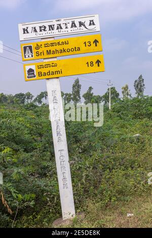 Pattadakai, Karnataka, Indien - 7. November 2013: Gelb und weiß Straßenschild gesponsert von Karnataka Tourismus zeigt auf Badami unter hellblauem Himmel und Stockfoto