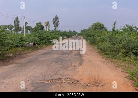 Pattadakai, Karnataka, Indien - 7. November 2013: Straße 14 mit mehr Schlaglöchern als flache Oberfläche und Schmutz an den Seiten östlich des Dorfes unter blauer Wolkenlandschaft Stockfoto