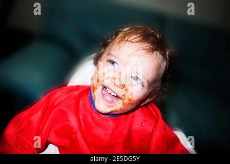 Glückliches Kleinkind mit Essen auf dem ganzen Gesicht lachend Stockfoto
