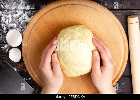 Der Prozess der Herstellung von Brotteig. Weibliche Hände halten den Teig. Der Teig steht auf dem Tisch. Flach Liegend. Stockfoto