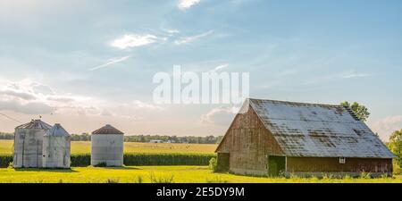 Landschaft mit verwitterten Scheune und Korn Mülleimer in den Vordergrund und Maisfeld, Bewässerungsanlagen und anderen landwirtschaftlichen Gebäude im Hintergrund Stockfoto