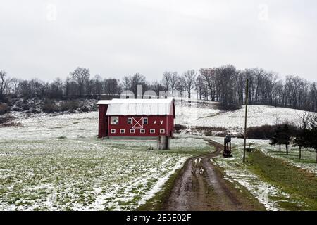 Schlammigen Weg führt zu einem roten Scheune auf einem verschneiten Hügel mit einem grauen bewölkten Himmel. Stockfoto