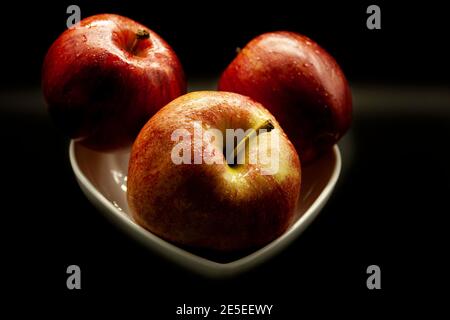 Drei frische Äpfel in einer weißen Schüssel auf einem angeordnet Schwarzer Hintergrund bereit zu essen Stockfoto