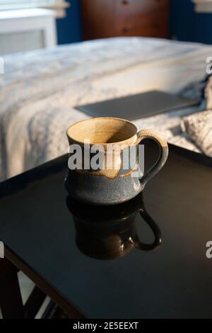 Teepause bei der Arbeit von zu Hause aus. Ein geschlossener Laptop steht auf dem Bett mit Teetasse Teetasse Tasse auf dem Nachttisch. Weitwinkelblick auf das Schlafzimmer, Büro, Stilleben Stockfoto