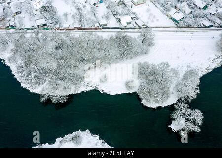 Winterlandschaft mit Dorf am See. Häuser am Ufer mit Schnee bedeckt. Luftbild