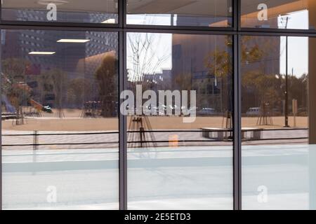 Verschwommenes Spiegelbild eines Parks, Autos und Gebäuden in den Fenstern eines anderen Gebäudes. Stockfoto