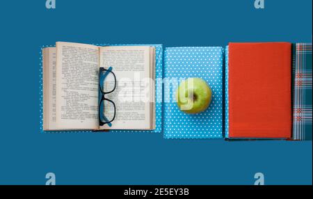 Offenes Lehrbuch, Bücherstapel in bunten Briefen und Apfel auf blauem Hintergrund. Zurück zur Schule Entfernung zu Hause Bildung. Stockfoto