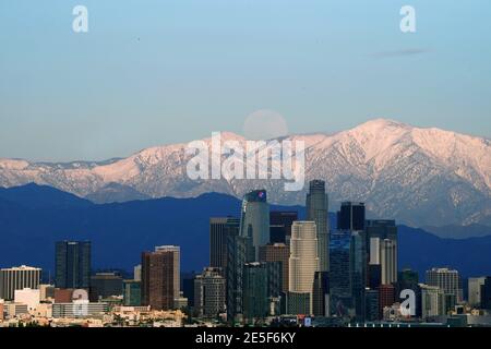 Am Mittwoch, den 27. Januar 2021, erhebt sich ein Vollmond über der Skyline der Innenstadt von Los Angeles mit den schneebedeckten San Gabriel Mountains als Kulisse. Stockfoto