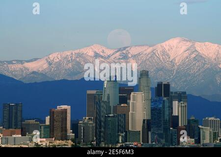 Am Mittwoch, den 27. Januar 2021, erhebt sich ein Vollmond über der Skyline der Innenstadt von Los Angeles mit den schneebedeckten San Gabriel Mountains als Kulisse. Stockfoto