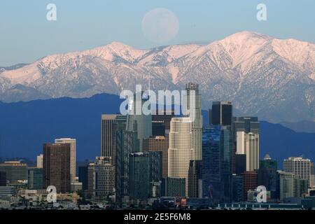 Am Mittwoch, den 27. Januar 2021, erhebt sich ein Vollmond über der Skyline der Innenstadt von Los Angeles mit den schneebedeckten San Gabriel Mountains als Kulisse. Stockfoto