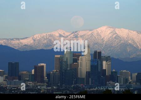 Am Mittwoch, den 27. Januar 2021, erhebt sich ein Vollmond über der Skyline der Innenstadt von Los Angeles mit den schneebedeckten San Gabriel Mountains als Kulisse. Stockfoto