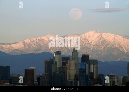 Am Mittwoch, den 27. Januar 2021, erhebt sich ein Vollmond über der Skyline der Innenstadt von Los Angeles mit den schneebedeckten San Gabriel Mountains als Kulisse. Stockfoto