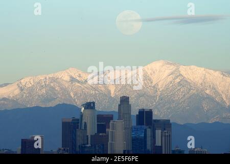 Am Mittwoch, den 27. Januar 2021, erhebt sich ein Vollmond über der Skyline der Innenstadt von Los Angeles mit den schneebedeckten San Gabriel Mountains als Kulisse. Stockfoto