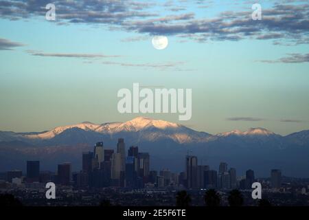 Am Mittwoch, den 27. Januar 2021, erhebt sich ein Vollmond über der Skyline der Innenstadt von Los Angeles mit den schneebedeckten San Gabriel Mountains als Kulisse. Stockfoto