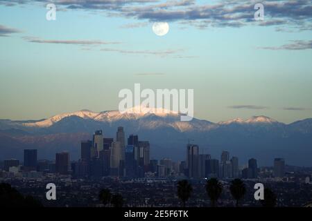 Am Mittwoch, den 27. Januar 2021, erhebt sich ein Vollmond über der Skyline der Innenstadt von Los Angeles mit den schneebedeckten San Gabriel Mountains als Kulisse. Stockfoto