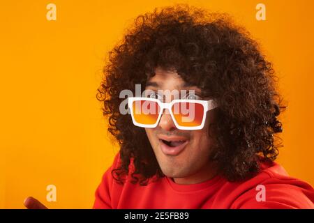 EIN JUNGER MANN MIT LOCKIGEN HAAREN, DER EINE BRILLE TRÄGT UND AUSSIEHT MIT ÜBERRASCHUNG WEG Stockfoto