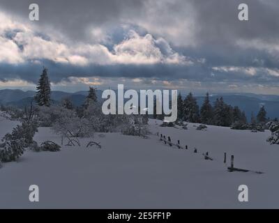 Wunderschöne Winterlandschaft mit Holzzaun bedeckt von tiefem Schnee, gefrorenen Bäumen und herrlichem Panoramablick über die Niedergebirge Schwarzwald. Stockfoto