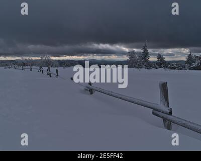 Atemberaubende Winterlandschaft mit Holzzaun bedeckt von tiefem Schnee, gefrorenen Bäumen und schöner Aussicht auf Schwarzwälder Hügel am Horizont. Stockfoto