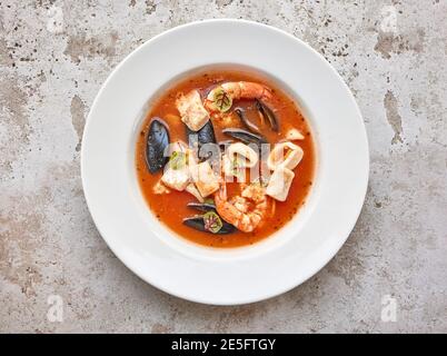 Portion Tomatensuppe mit Meeresfrüchten auf weißem Teller Anzeigen Stockfoto