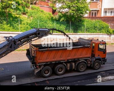 Die Fräsmaschine entfernt alten Asphalt von der Straße und transportiert ihn zu einem LKW. Stockfoto