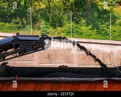 Die Fräsmaschine entfernt alten Asphalt von der Straße und transportiert ihn zu einem LKW. Eine detaillierte Ansicht des Transportbandes. Stockfoto
