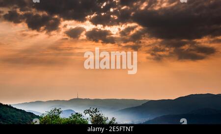 Dunkle Morgenwolken mit Sonnenstrahlen und Nebel in der Tal - am Horizont ist die Umrisse der Funkturm Stockfoto