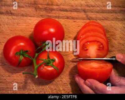 Tomatenscheiben mit einem Messer auf einem Holzhintergrund Stockfoto