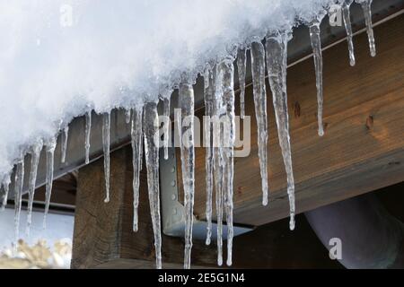 Draußen im Winter hängen lange Eiszapfen von den Dachsparren Stockfoto