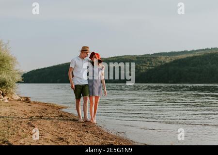 Ein Paar, das sich verliebt hat, läuft am schönen Sommerabend am Strand entlang. Portrait von jungen Frau und Mann umarmt, während gehen für Spaziergang auf dem Be Stockfoto