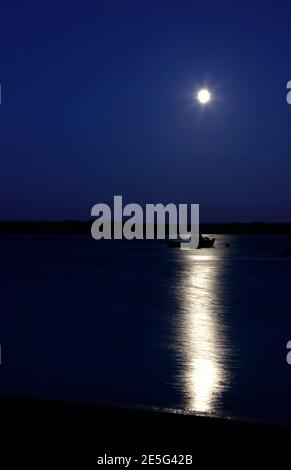 Fischerboot beleuchtet vom Mond in Wells Salt Marshes, Wells-Next-the-Sea, Norfolk, England, Großbritannien Stockfoto