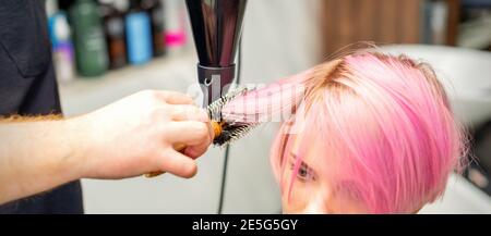 Friseur trocknet rosa Haar der jungen Frau in einem Schönheitssalon Stockfoto