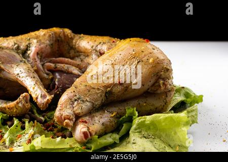 Rohes Kaninchenfleisch in Gewürzen auf Salatblättern. In Gewürzen, Zitronensaft, Pfeffer und Knoblauch marinieren Stockfoto