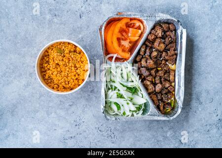 Türkische Take Away Kebab Leber mit Zwiebeln und Tomaten in Tabldot Folie Platte. Serviert mit Bulghur oder Bulgur Reis Pilav Pilaf. Bereit zum Essen. Stockfoto