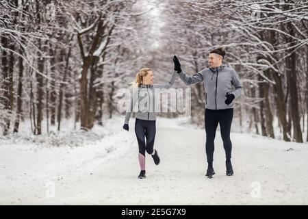 Sportliches Paar läuft zusammen an verschneiten Wintertagen im Wald. Sie geben einander hohe fünf. Outdoor-Fitness, Winter-Fitness, gesunde Gewohnheiten Stockfoto