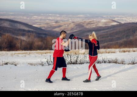 Sportlerin Sparring mit Boxhandschuhen in der Natur an verschneiten Wintertagen mit ihrem Trainer. Boxen, Winterfitness, Outdoor Fitness Stockfoto