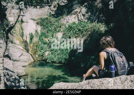 Mädchen sitzt auf einem Felsen Blick auf eine Landschaft von Ein kleiner Wasserfall an einem sonnigen Tag Stockfoto