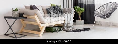 Graue Knoten Kissen auf einem hölzernen Sofa in White room Einrichtung mit grünen Pflanzen und runde Stuhl gelegt Stockfoto