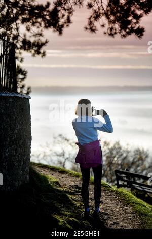 Ein Jogger hält an, um die nebligen Ansichten aus dem aufzuzeichnen Cotswold Escarpment in der Nähe von Wotton-under-Edge in Gloucestershire in Richtung Bristol UK Stockfoto