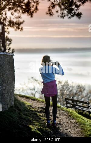 Ein Jogger hält an, um die nebligen Ansichten aus dem aufzuzeichnen Cotswold Escarpment in der Nähe von Wotton-under-Edge in Gloucestershire in Richtung Bristol UK Stockfoto